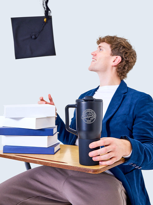 Boy throwing graduation cap in the air holding a Müv tumbler.