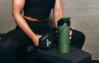 A woman sitting on a workout bench with an OD Green MultiShaker in her left hand